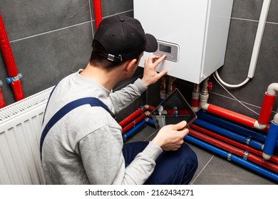 De technicus die het verwarmingssysteem in de stookruimte controleert met een tablet in de hand