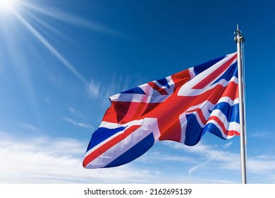 Close-up van een nationale Britse vlag met vlaggenmast, waait in de wind op een blauwe lucht met wolken, zonnestralen en kopieerruimte. Union Jack-vlag.