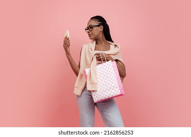 ファッショナブル。ピンクの背景に分離されたショッピング バッグを保持しているカジュアルなスタイルの服装でアフロの髪型を持つ魅力的な少女の肖像画。美しさ、芸術、若さ、販売、広告のコンセプトです。広告用のコピー スペース
