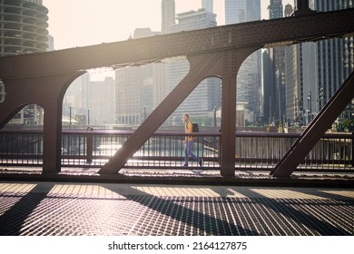 Side view of man on the move while walking on bridge and looking around. City in morning light. 