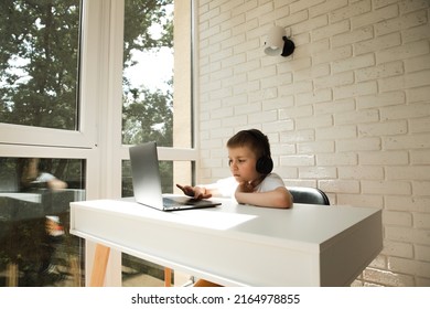 大きなヘッドフォンの窓の近くの白いテーブルで 6-7 歳の男の子はラップトップを使用します