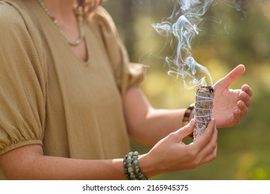 occult science and supernatural concept - close up of woman or witch with smoking white sage performing magic ritual in forest