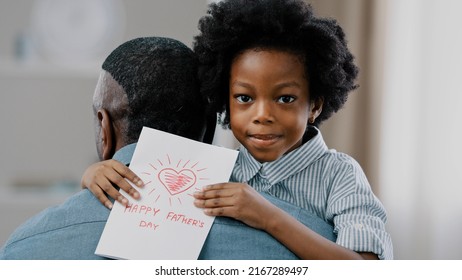 クローズアップのかわいい笑顔の子供の女の子は、休日を祝うお父さんを抱きしめます思いやりのある娘は、最愛のお父さんに手作りのカードを渡します