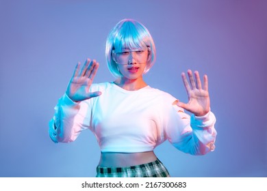 Fille cyberpunk asiatique avec une coiffure courte bleue portant des lunettes cyber vr posant la main touchant l'arrière-plan de l'écran couleur violet néon. Concept de métaverse.