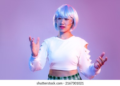 Femme cyberpunk asiatique aux cheveux courts bleus portant des lunettes de réalité virtuelle cybernétique posant comme un robot sur un fond d'écran couleur violet fluo. Concept de métaverse.