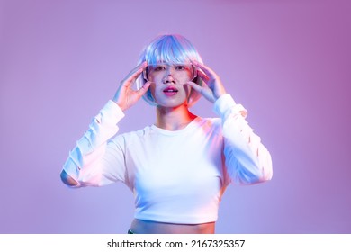 Fille cyberpunk asiatique avec une coiffure courte bleue portant des lunettes cyber vr posant sur un fond d'écran couleur violet néon.