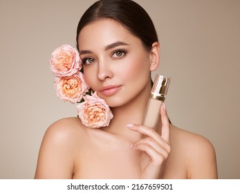 Retrato hermosa mujer joven con piel limpia y fresca. Modelo con botella de maquillaje base. Hermosa mujer joven con una flor color de rosa