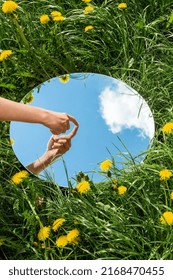 Naturkonzept - Hand, die die Himmelsreflexion im runden Spiegel auf dem Sommerfeld berührt