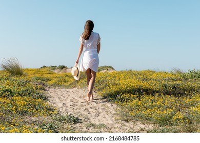 Quay lại cảnh người phụ nữ đi chân trần cầm mũ rơm khi đi dạo trên bãi biển