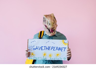 Man with lizard mask on pink background with sign that says save the planet.