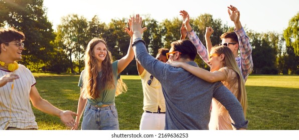 Stelletje gelukkige jonge vrienden die allemaal samen plezier hebben op een warme zonnige dag in het zomerpark. Diverse groep vrolijke vrolijke positieve mensen die op een groen gazon staan, glimlachen en elkaar high five geven