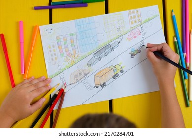 Child draws a pencil drawing of the city, cars and air pollution. Top view.