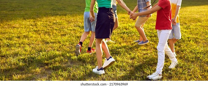 Kleine kinderen die leuke spelletjes buiten spelen. Gelukkige jongens en meisjes dansen ronde dans op groen gras in het park. Bijgesneden geschoten kinderbenen. Verschillende onherkenbare vrienden hand in hand en dansen in een cirkel