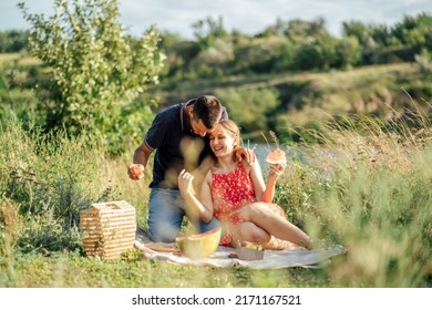 Junges verliebtes Paar beim Sommerpicknick mit Wassermelone. Liebespaar sitzt am Fluss, redet, lächelt, lacht, isst Wassermelone
