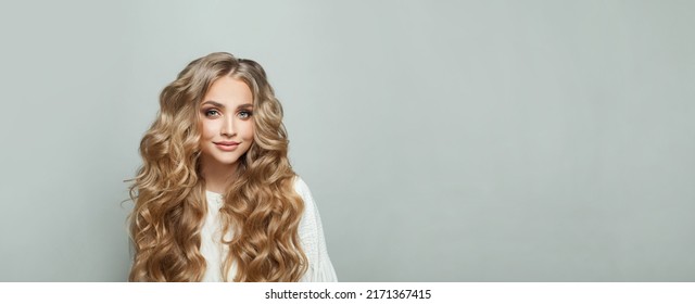 Una joven rubia atractiva y alegre con el pelo largo y sedoso y ondulado sonriendo contra el fondo blanco de la pancarta en la pared del estudio con espacio para copiar