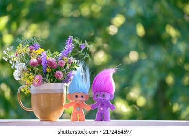 ramo de flores en taza y trolls de juguetes de cerca sobre fondo natural abstracto. composición floral. temporada primavera verano. concepto de amistad