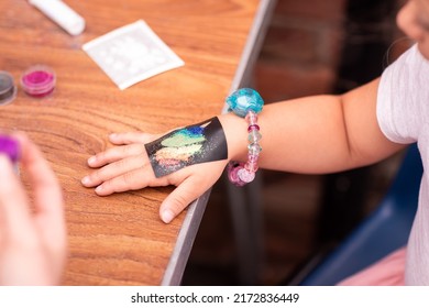 Little girl getting glitter tattoo at birthday party. Shimmering sparkling tattoo on a child's hand. Body art