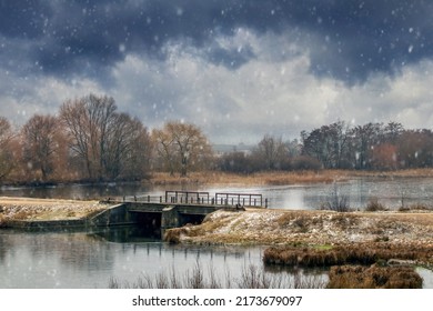 Paisaje invernal con un puente sobre ríos, árboles a orillas del río y un cielo oscuro y nublado durante las nevadas. Comienzo del invierno, nevadas