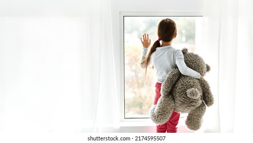 Sự cô đơn. Cô gái mồ côi cô đơn trong trại trẻ mồ côi nhìn ra ngoài trong khi ôm gấu bông bên cửa sổ. Khái niệm cảm xúc trẻ em