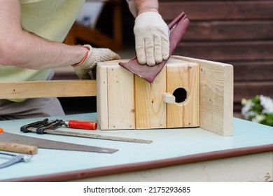 Close-up van een ambachtsman die een houten vogelhuisje maakt met gereedschap. DIY-concept. Timmerman polijst nestkast met schuurpapier.
