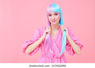 Een lief lachend meisje met gekleurd paarsblauw haar gekleed in een roze jurk poseert op een roze achtergrond. Kapsel, haarkleuring. Make-up en cosmetica.