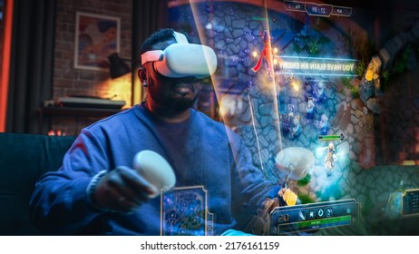 Retrato cinematográfico de un joven negro elegante que lleva un casco de realidad virtual. Hombre afroamericano sentado en un sofá en casa jugando a un juego de realidad virtual. Visualización del concepto de juego.