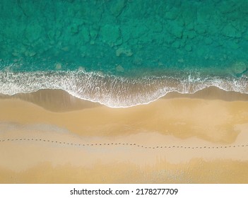 Human footprints on a sandy shore along the sea with breaking waves. Aerial view directly above