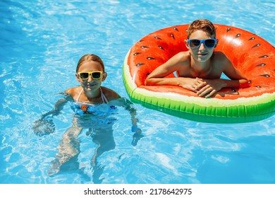 jongen en een meisje in zonnebril zwemmen in het buitenzwembad. Zomervakantie met kinderen. Zwemhulpmiddelen en kinderkleding. water speelgoed. Een klein kind drijft op een kleurrijk vlot.