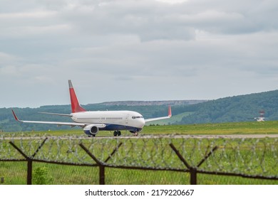ターボジェットエンジンを搭載した民間旅客機が、曇りの天候で有刺鉄線のフェンスを背景に、空港の滑走路に沿って加速する