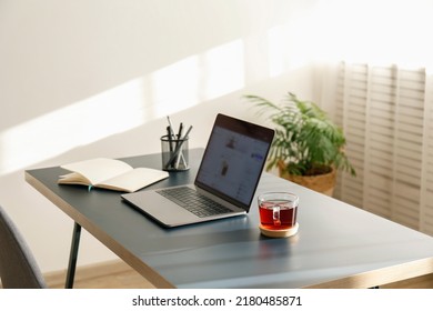 Conceito de escritório em casa. Área de trabalho designada perto da janela. Laptop moderno com tela desfocada e xícara de chá de vidro sobre a mesa. Close-up, espaço para texto, fundo de ambiente interno.