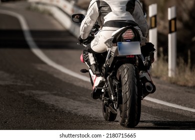 bagfra af en ung motorcykelkvinde klædt i en læderbeskyttelsesdragt og sikkerhedshjelm, der kører på sin motorcykel på en asfaltvej