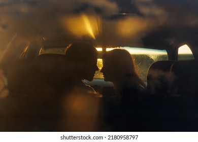Silueta de una pareja joven a la luz del atardecer besándose en un auto