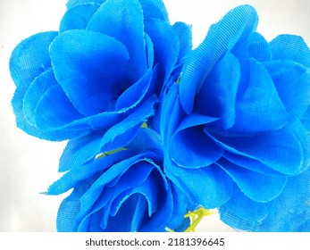 A blue ornamental flower whose petals are made of cloth and the stem is made of plastic on an isolated white background