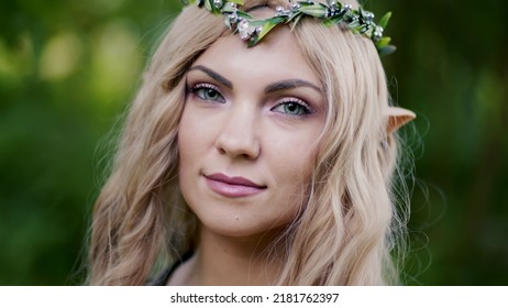 Portrait of young woman in cosplay elf clothes with make-up on green background. Fantastic look, long blonde hair, forest crown. Halloween concept. High quality photo