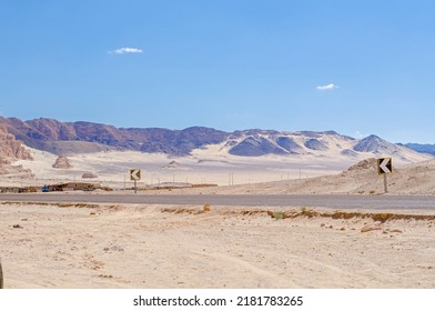 岩山と黄砂の丘のある広大な砂漠に建設されたアスファルト高速道路。真っ青な空の下の美しい野生の自然と道路標識