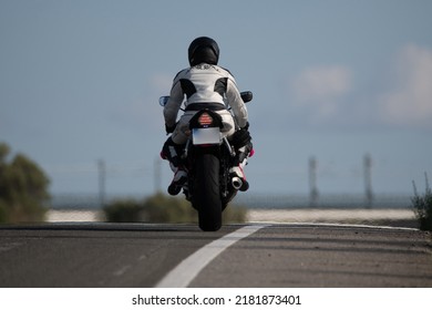 bagfra af en ung motorcykelkvinde klædt i en læderbeskyttelsesdragt og sikkerhedshjelm, der kører på sin motorcykel på en asfaltvej