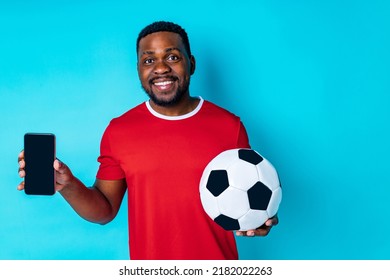 hombre hispano latino con teléfono y pelota de fútbol en el fondo azul del estudio