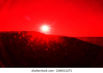 海岸 (丘と海) に光線と太陽フレア (「スポット突起」) を持つ夕日の円盤。超現実的な芸術の赤外線写真