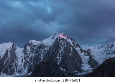 Atmospheric landscape with sunset pink reflection on huge snowy mountain top in dramatic sky. Hanging glacier and cornice on giant snow mountains in dusk. High snow-covered mountain range in twilight.