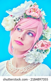 A beautiful girl with bright pink makeup and pink hair poses in floral wreath on her head. Japanese anime style. Spring and summer beauty. Blue background. Beauty girl. 