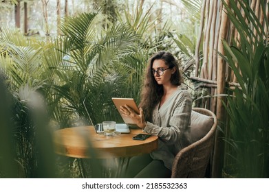 امرأة جميلة تستخدم جهازًا لوحيًا مع قلم رصاص في مقهى، ترسم الرسوم التوضيحية، حالمة، تشرب القهوة، تستخدم الهاتف الذكي، مزاجات المستقلين، الكمبيوتر المحمول، الهيبستر، الفن، مجموعة NFT، النظارات، بالي، المفهوم