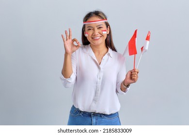 Wanita muda Asia tersenyum memegang bendera Indonesia sambil menunjukkan gerakan yang baik terisolasi di latar belakang putih. Konsep hari kemerdekaan Indonesia