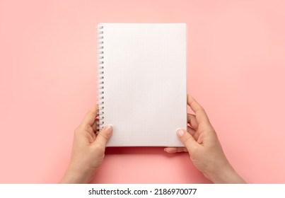 Maqueta de bloc de notas. manos femeninas sosteniendo un bloc de notas en espiral en blanco o un calendario sobre fondo de mesa rosa. las manos muestran un cuaderno abierto. Manos femeninas sosteniendo un cuaderno blanco en blanco. copie el espacio