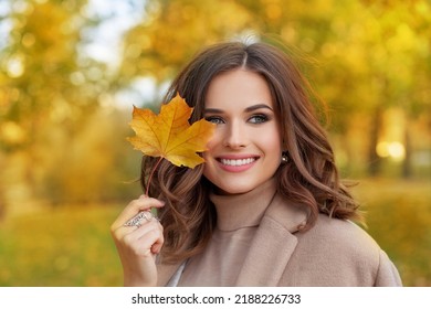 色鮮やかな紅葉の近くに立っている美しい秋の女性のポートレート、クローズ アップ。カメラを見てかなり幸せな陽気なモデル。