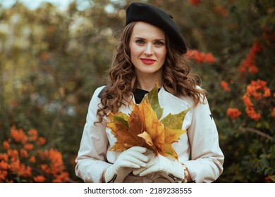 Hallo september. stijlvolle vrouw in beige trenchcoat met herfstgele bladeren buiten op straat in de stad in de herfst.