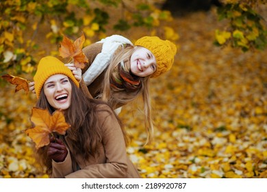 Hallo oktober. gelukkige jonge moeder en dochter in oranje hoeden met herfstgele bladeren die in de herfst plezier hebben buiten in het stadspark.
