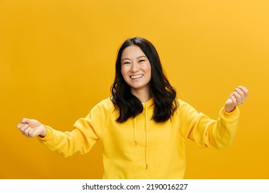 うん、やった。黄色のパーカー スウェット シャツを着た大喜びのアジア学生の若い女性は、オレンジ色のスタジオの背景に分離された笑顔のポーズを拳を上げます。クールなオファー。人々 の感情の概念