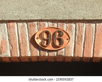 House number (address) ninety six (96) sign, black numbered plate (closeup) against red (orange) bricks wall of old building background. Grunge, texture, wallpaper