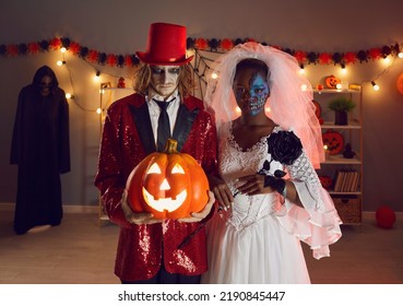 死んだ花嫁とジョーカーに扮した不気味な男女の不気味なハロウィーンのポートレート。ジャック・オ・ランタンを持つ白人男性と、暗闇の中で恐ろしい表情をした黒いバラのスタンドを持つ黒人女性