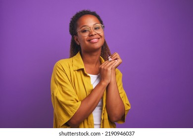 若い魅力的な長髪のアフリカ系アメリカ人女性ミレニアル世代のスタイリッシュな眼鏡をかけたカメラはかわいく見え、恥ずかしそうにポジティブな感情を表現し、紫色のスタジオでポーズをとる自然な美しさを持っています